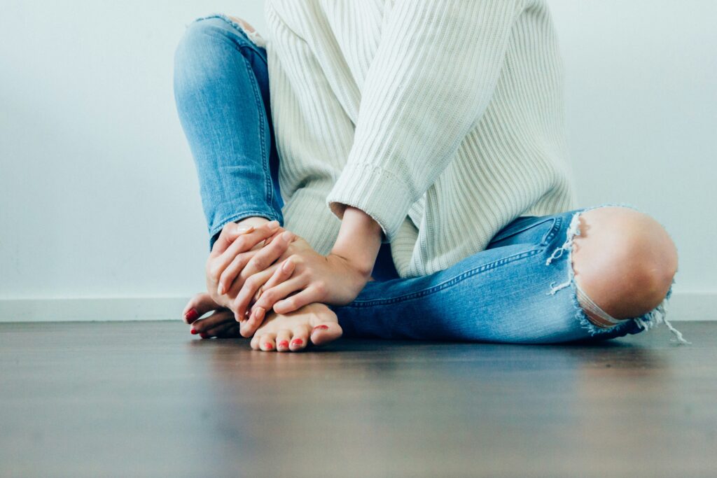 A young woman in a white blouse holds her right ankle tightly with both hands