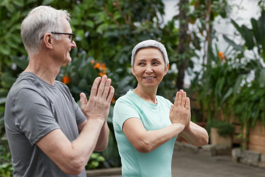 An adult man and woman are doing exercise togethe in nature and smiling each other